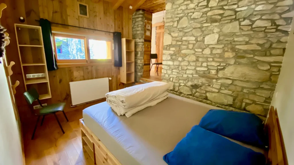 Chambre avec lit double et mur en pierre, ambiance chaleureuse et authentique dans un appartement en montagne