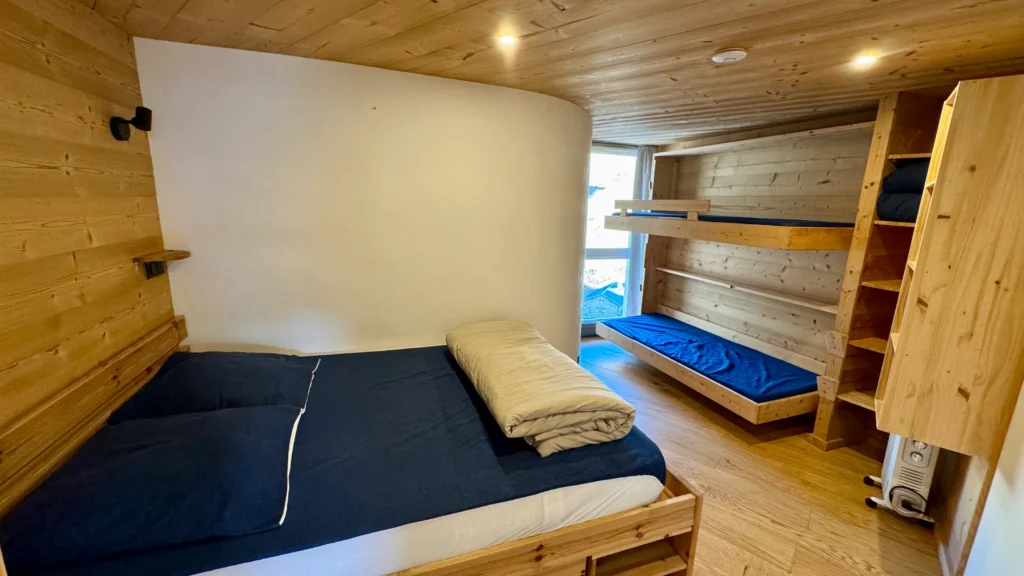 Chambre en bois avec lit double et deux lits simples, ambiance chaleureuse et authentique dans un espace confortable et bien agencé