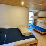 Chambre en bois avec lit double et deux lits simples, ambiance chaleureuse et authentique dans un espace confortable et bien agencé