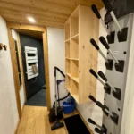Couloir menant à la salle de bain avec sèche-chaussures de ski et aspirateur, espace pratique et fonctionnel pour l’entretien et le retour du ski