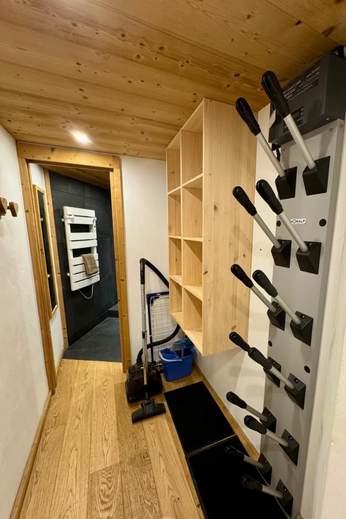 Couloir menant à la salle de bain avec sèche-chaussures de ski et aspirateur, espace pratique et fonctionnel pour l’entretien et le retour du ski