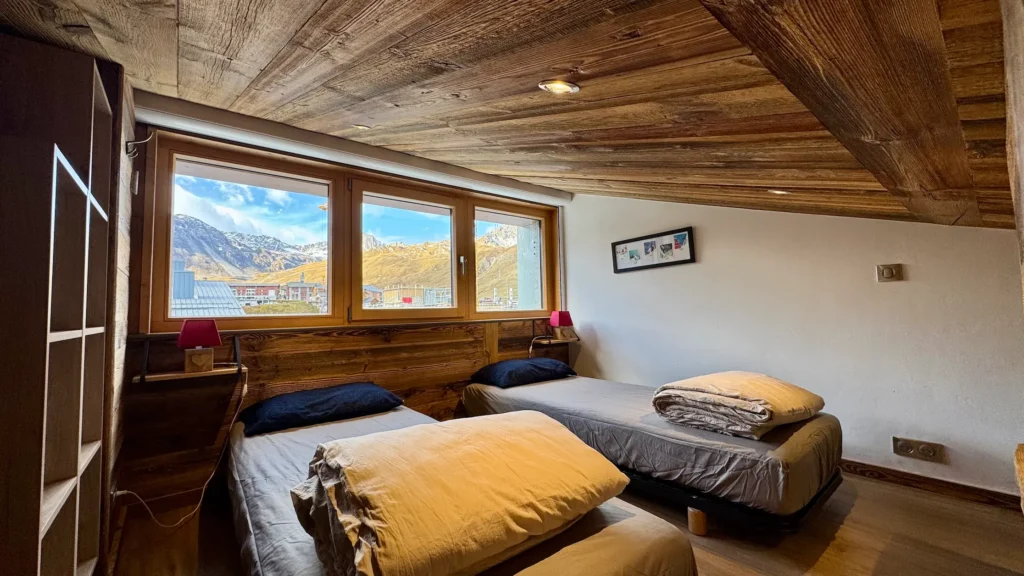 Chambre avec deux lits simples vue sous un autre angle, fenêtre offrant une vue sur la montagne et ambiance lumineuse et apaisante