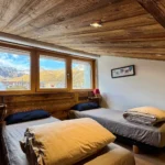 Chambre avec deux lits simples vue sous un autre angle, fenêtre offrant une vue sur la montagne et ambiance lumineuse et apaisante