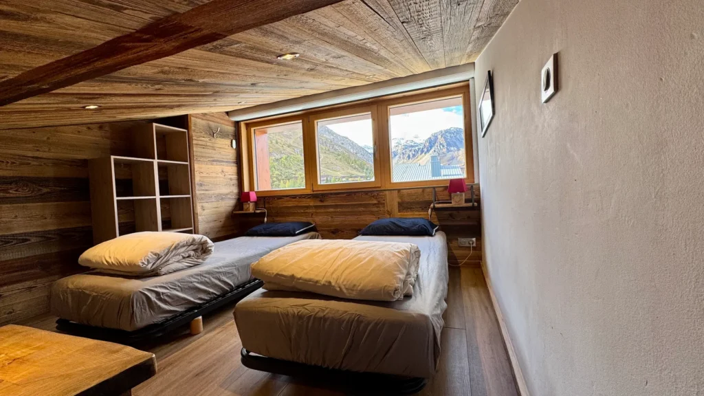 Chambre avec deux lits simples et fenêtre donnant sur une vue sur la montagne, espace lumineux et calme idéal pour un séjour reposant