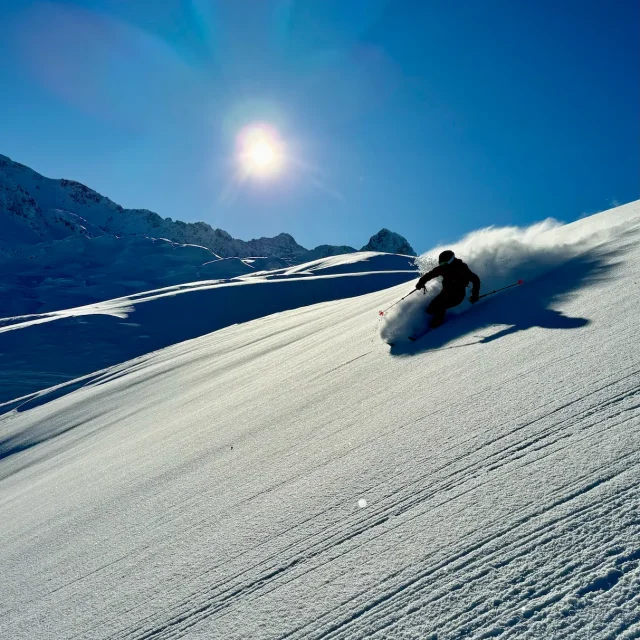 Skieur en descente freeride dans la poudreuse sous un grand ciel bleu