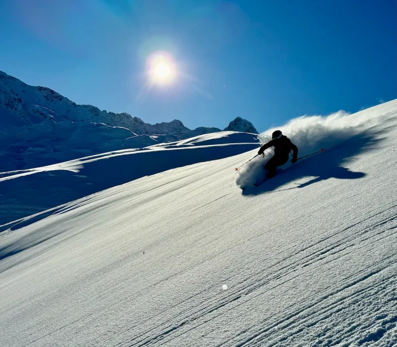 Skieur en descente freeride dans la poudreuse sous un grand ciel bleu